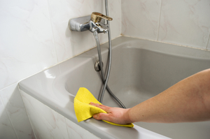 Женщина чистит чугунную ванну в резиновых перчатках
